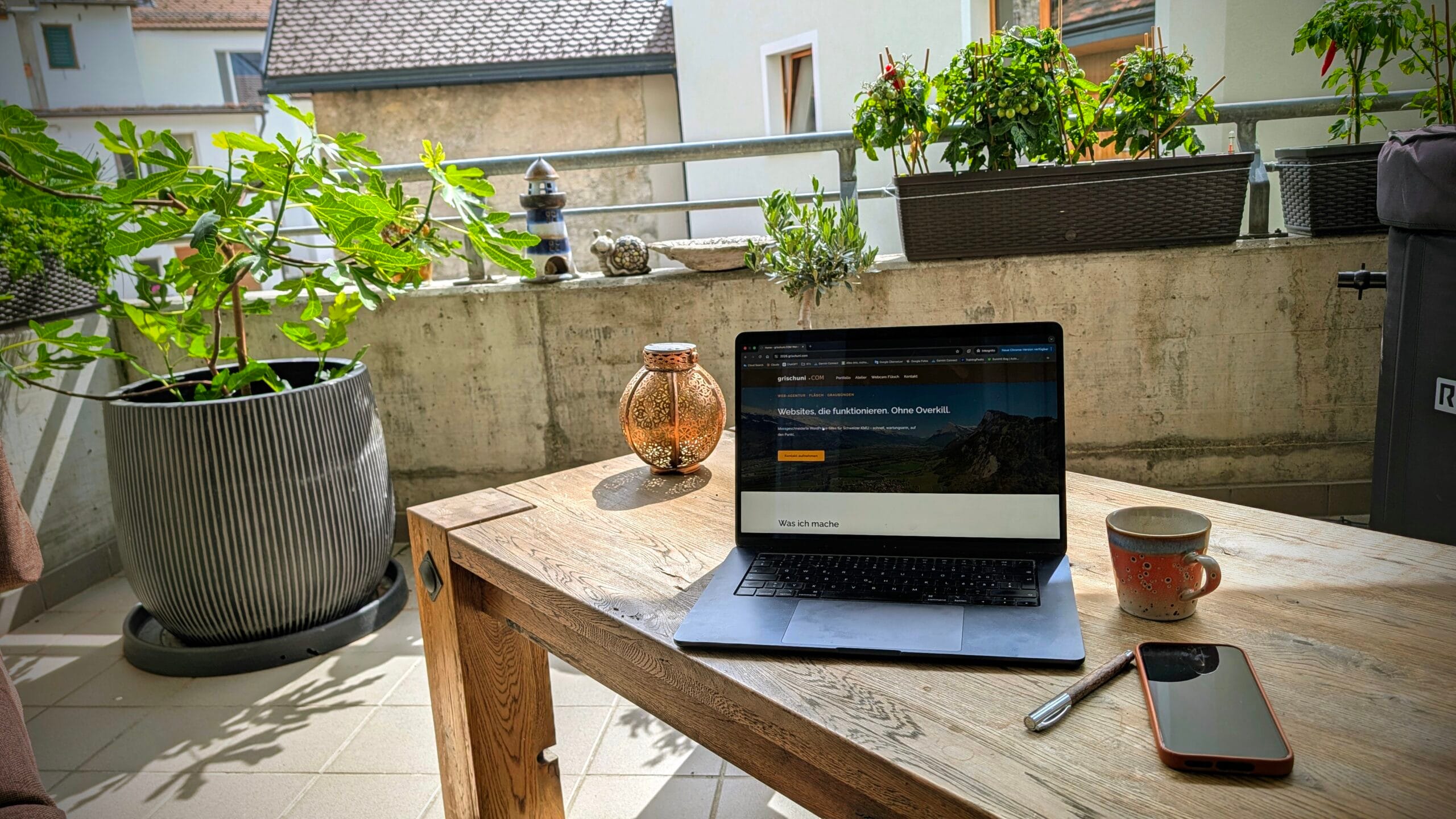 Laptop auf Holztisch auf Balkon mit Pflanzen, Tasse und Smartphone
